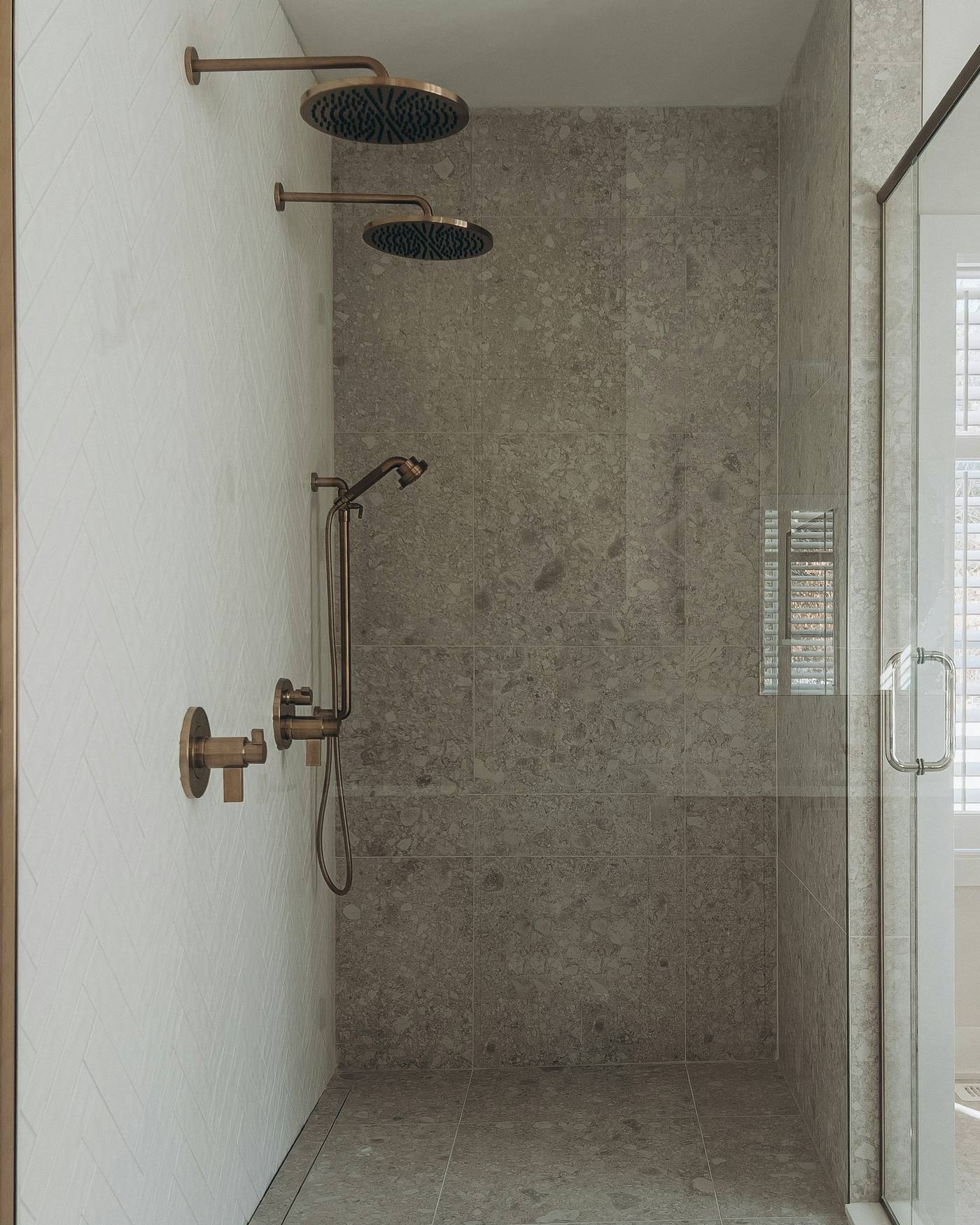 A walk-in shower with brushed brass shower heads and terrazzo-style tiles