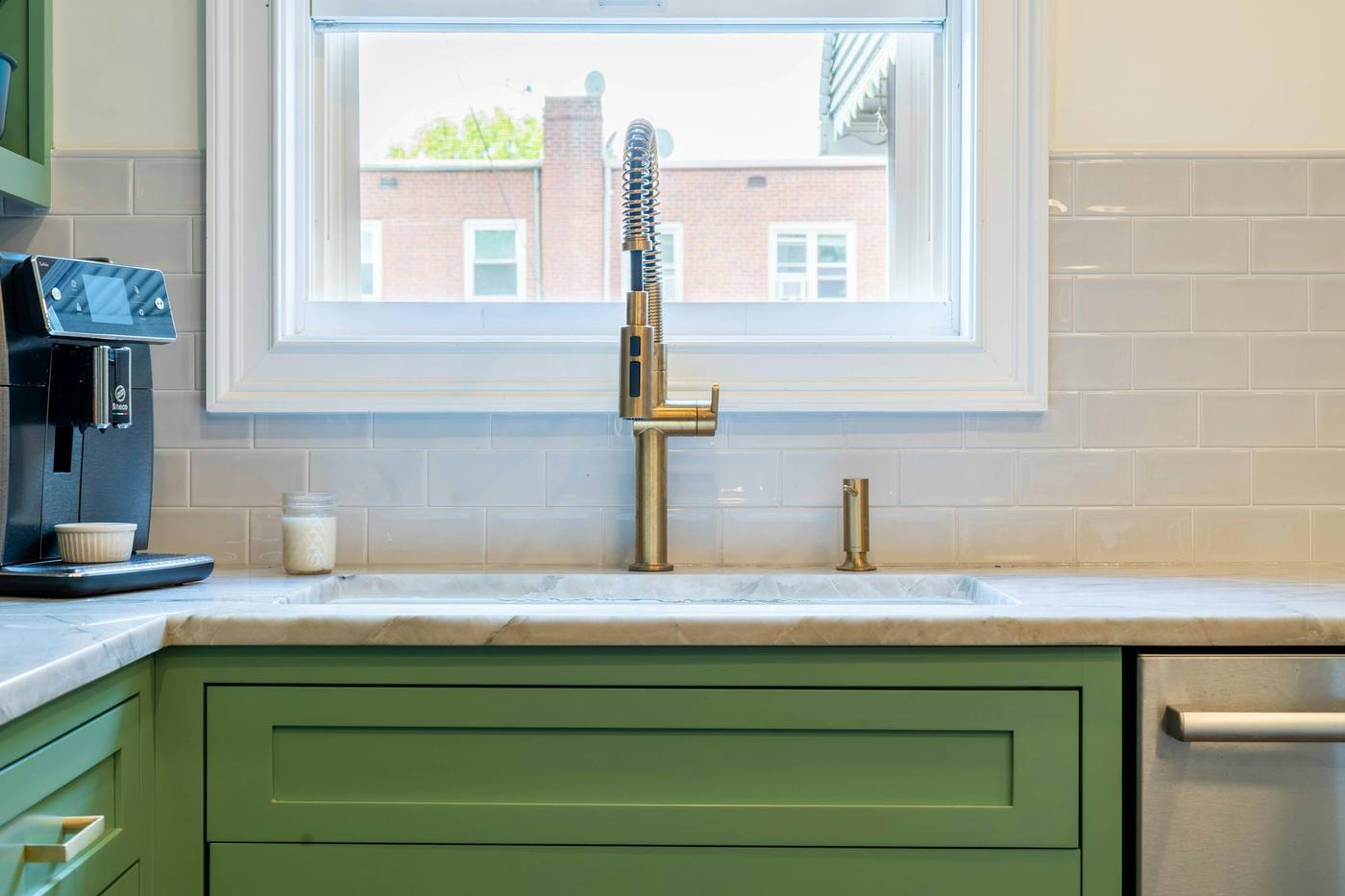 A sage green shaker kitchen with brass handles, a brass tap and a tiled splashback